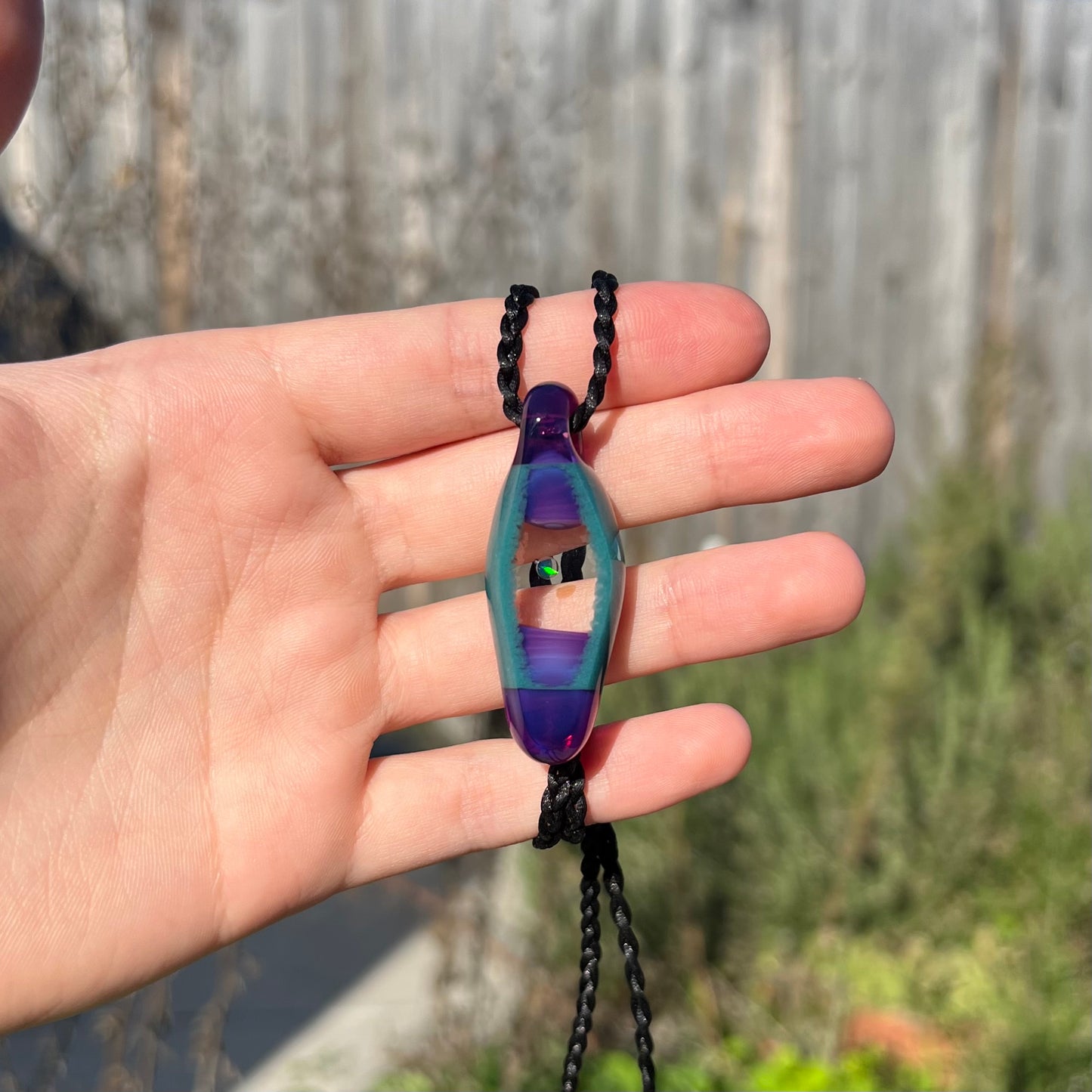 A unisex boro glass and opal necklace with a green flash of color play, held in a hand and shown in the sunlight.
