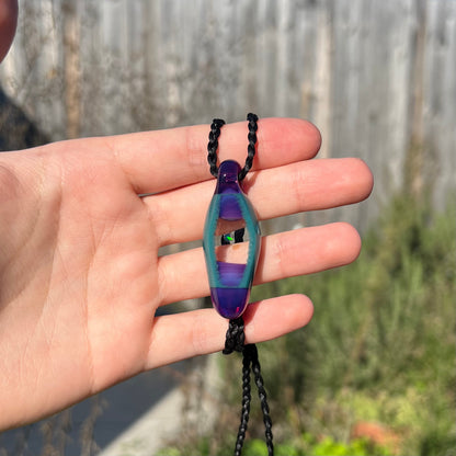 A unisex boro glass and opal necklace with a green flash of color play, held in a hand and shown in the sunlight.