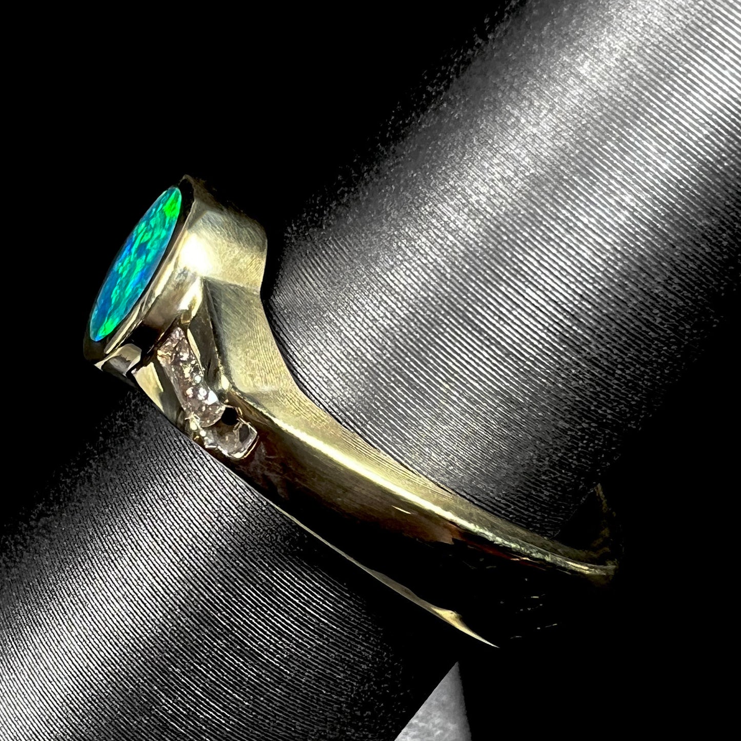 Side view focusing on the Euro shank of a unisex 18k yellow gold boulder opal ring, shown close-up on a ring display.