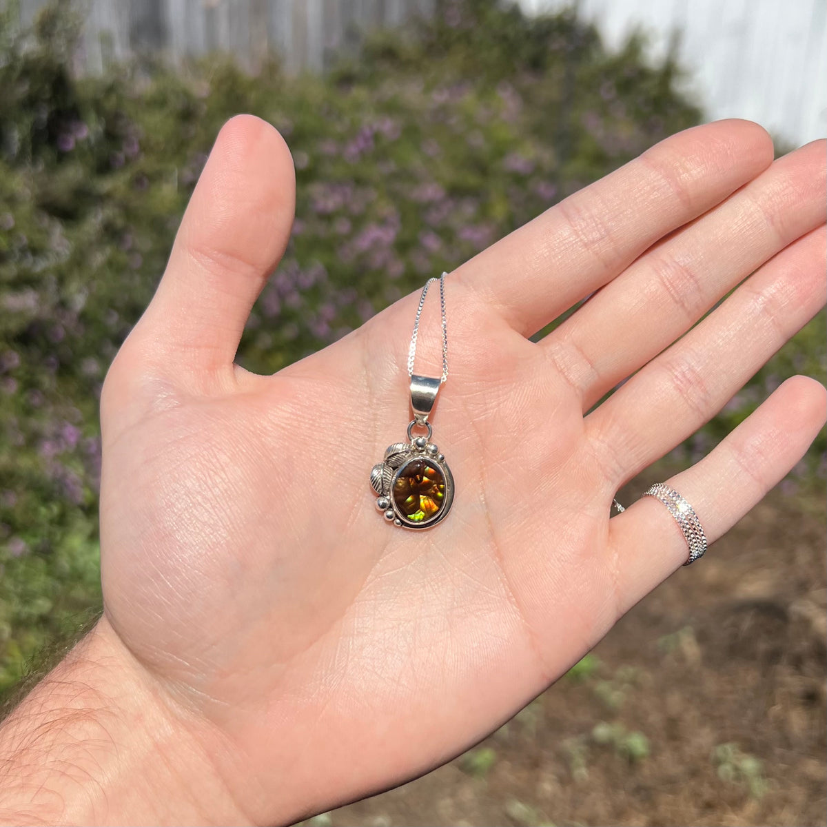 Hand holding a unisex sterling silver fire agate necklace in natural sunlight against blurred outdoor background.
