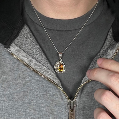 Close-up of person's neck and chest region wearing unisex fire agate necklace in sterling silver against dark shirt beneath partially unzipped hoodie.