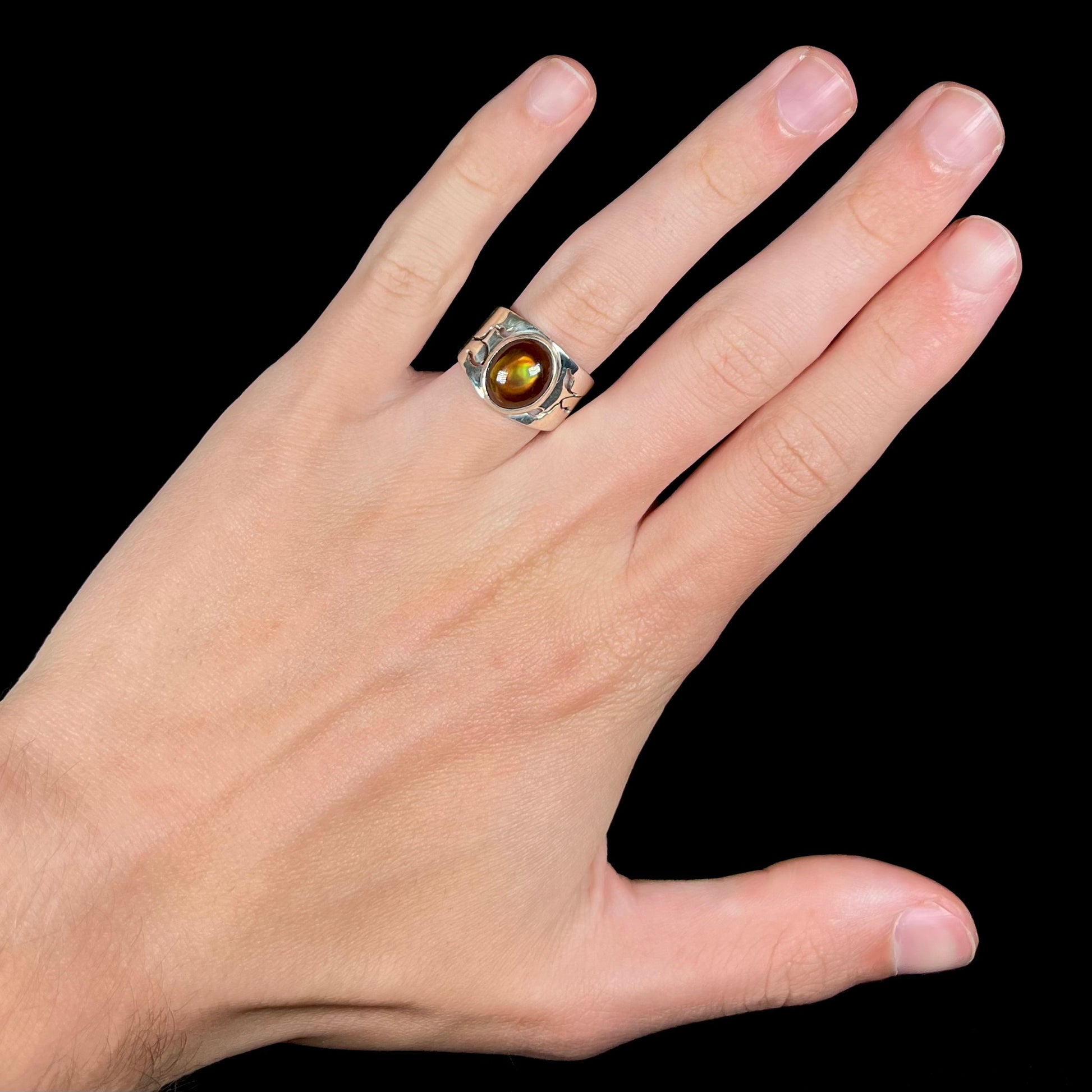 A unisex Mexican fire agate ring made from sterling silver worn on a hand against a black background.