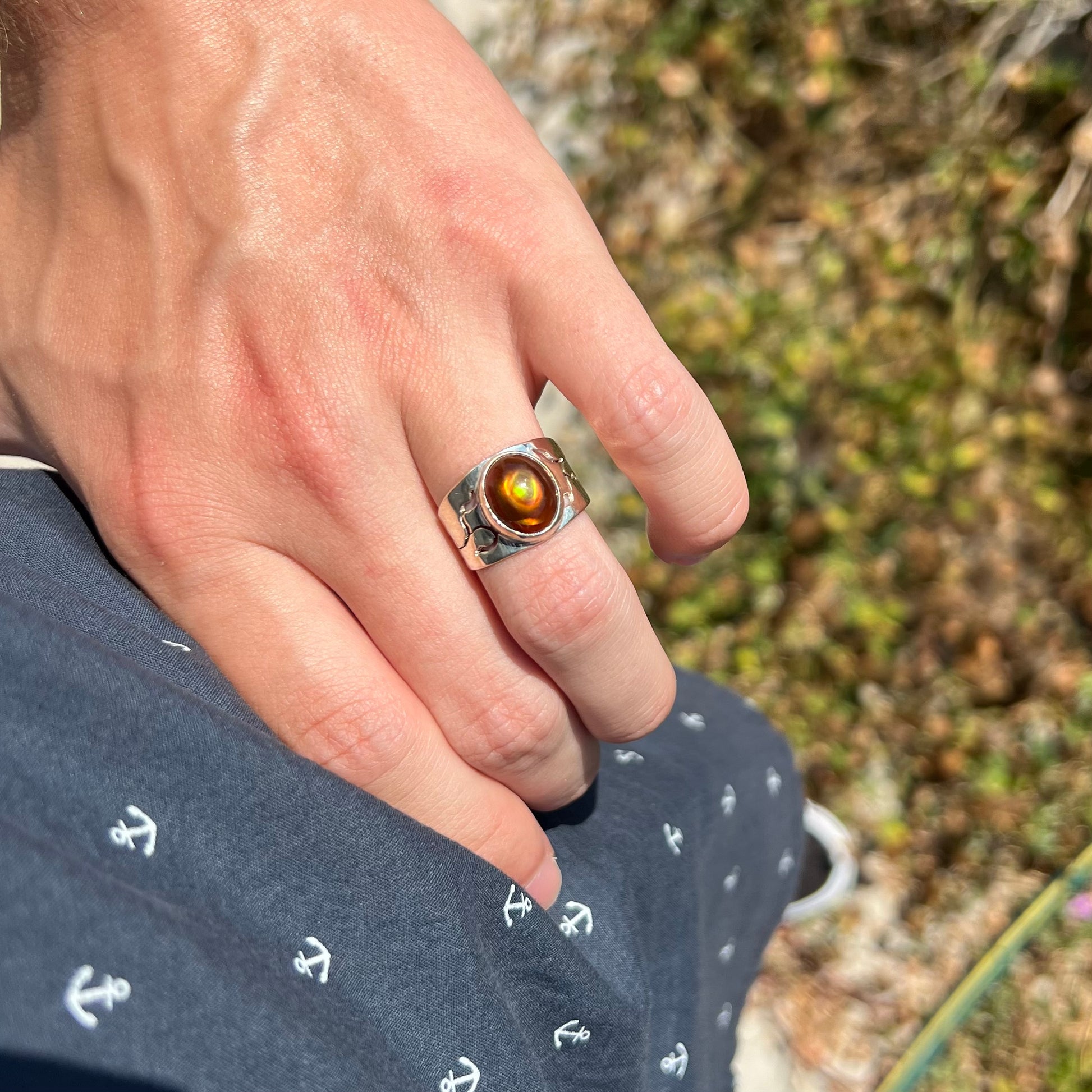 A hand resting on a hip in the sunlight while wearing a silver unisex fire agate ring with a wide band.