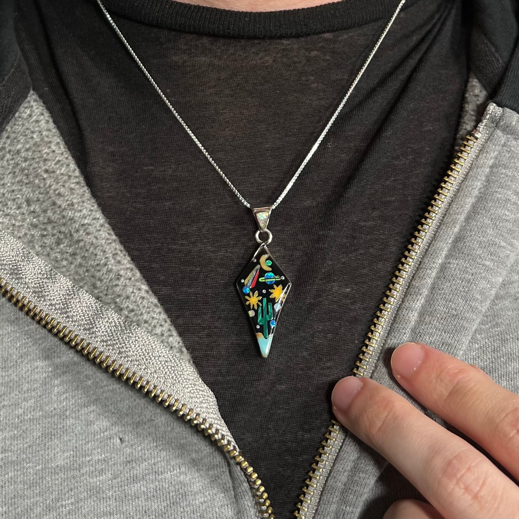 Man wearing unisex Southwest gemstone inlay necklace with planet and cactus motif against dark shirt under hoodie.