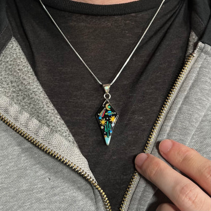 Man wearing unisex Southwest gemstone inlay necklace with planet and cactus motif against dark shirt under hoodie.