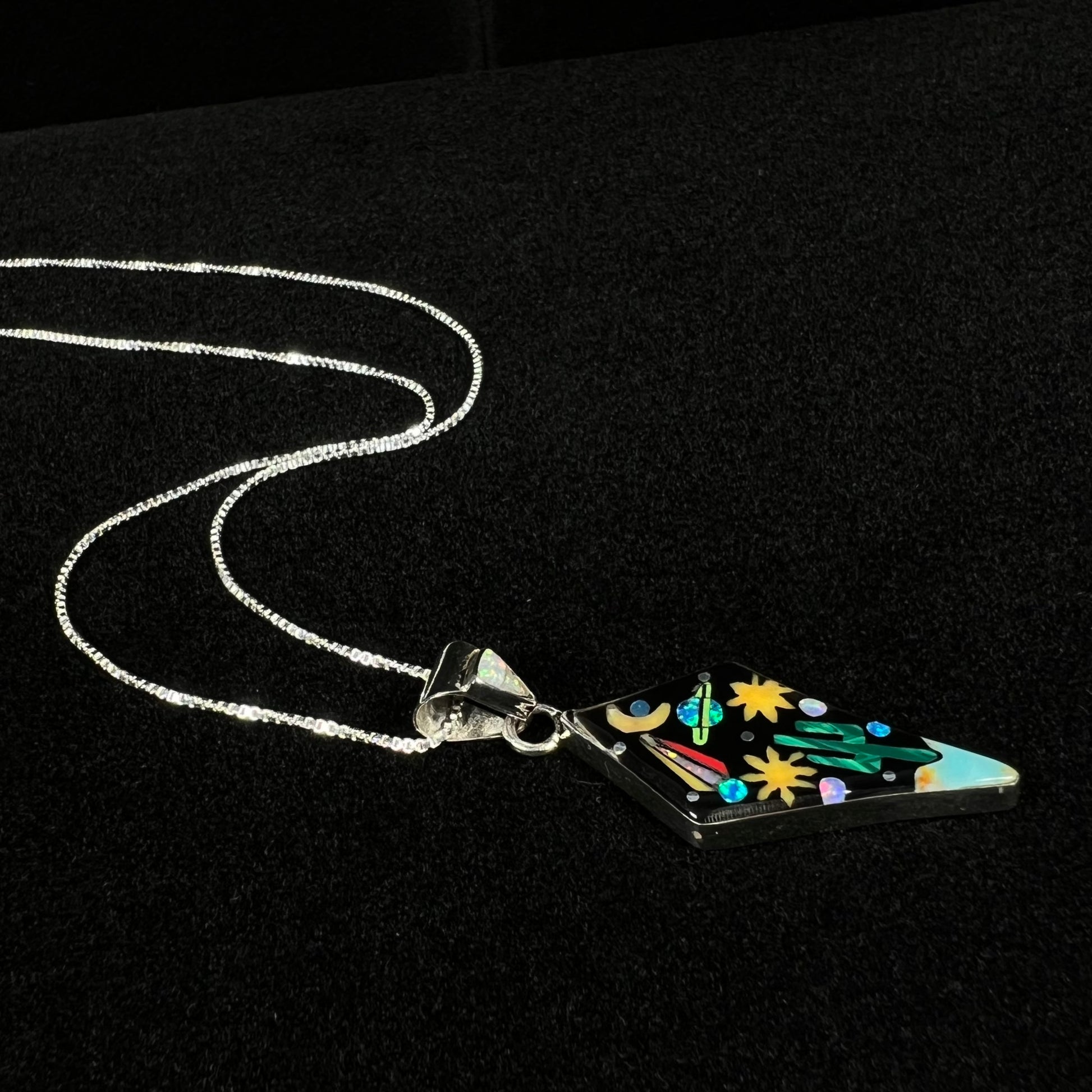 A unisex Southwest-style inlay necklace with space and cactus motif shown from an angle laying on dark felt.