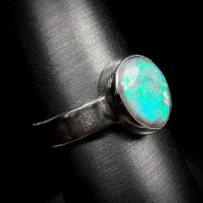 Angled macro view of a unisex sterling silver Australian opal solitaire ring with a bright blue flash of color, shown on a ring display.