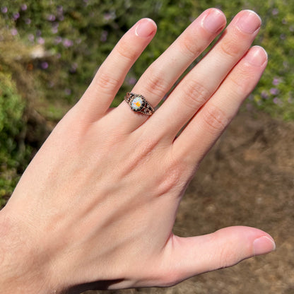 Hand wearing a used, estate Australian opal in brass ring under natural sunilght; the opal has a bright red flash of color, seen from a distance
