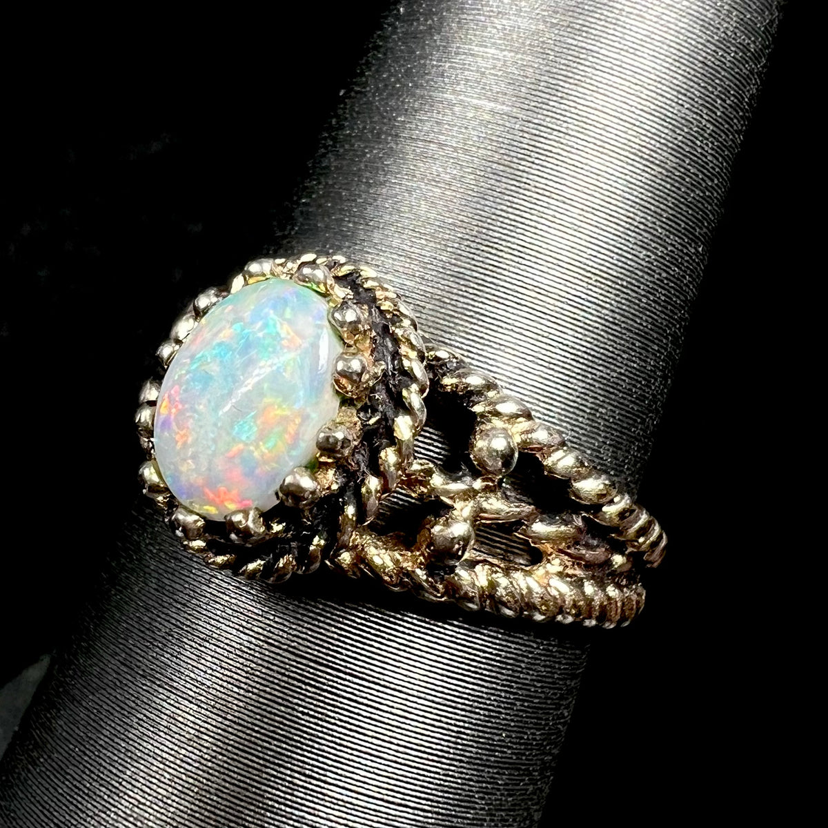 Close-up angled view of a used brass ring prong-set with a natural Australian opal, shown on a ring display
