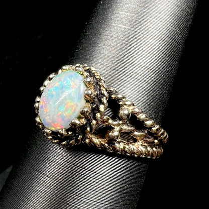Close-up angled view of a used brass ring prong-set with a natural Australian opal, shown on a ring display