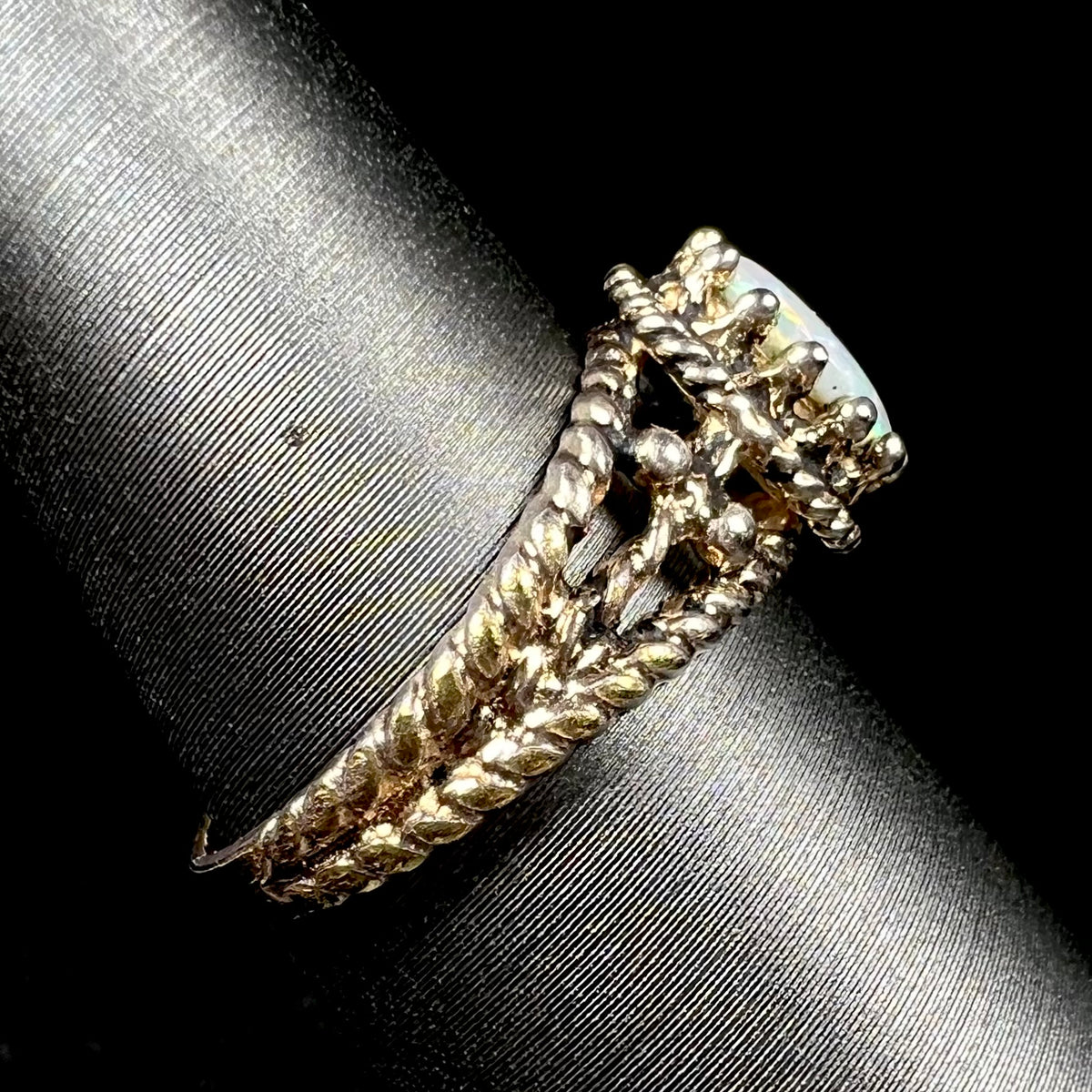 Side view of a used, estate brass Australian opal ring on a ring display; the ring's shank has a twisted rope design, and its prongs have a crown design