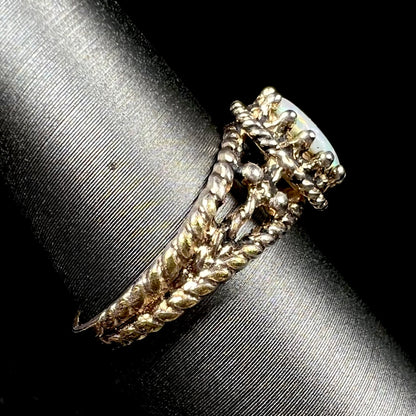 Side view of a used, estate brass Australian opal ring on a ring display; the ring's shank has a twisted rope design, and its prongs have a crown design