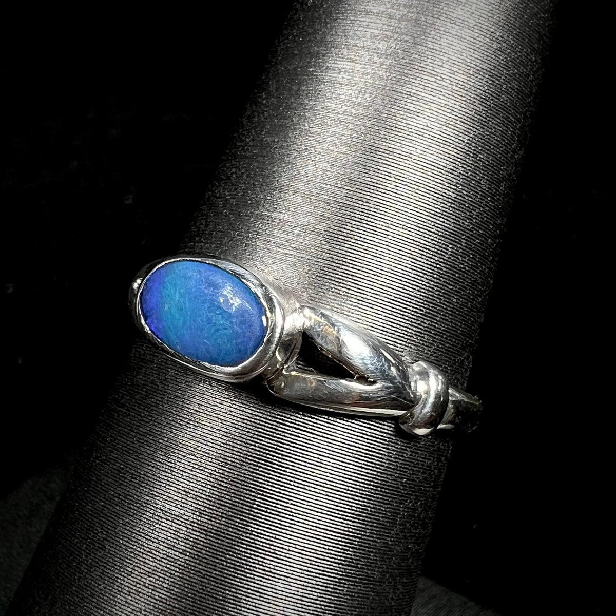 Angled close-up of used blue Australian opal doublet solitaire ring in sterling silver, shown on ring display