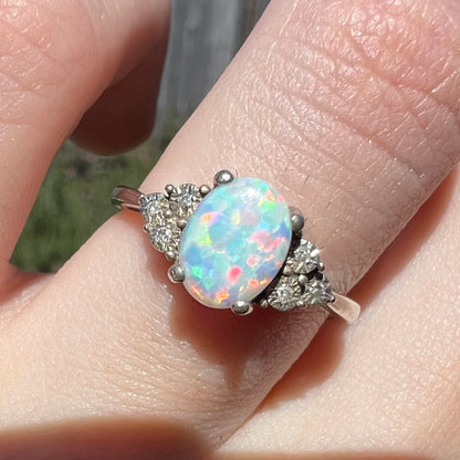Close-up of used sterling silver opal and diamond engagement ring worn on finger in natural sunlight.