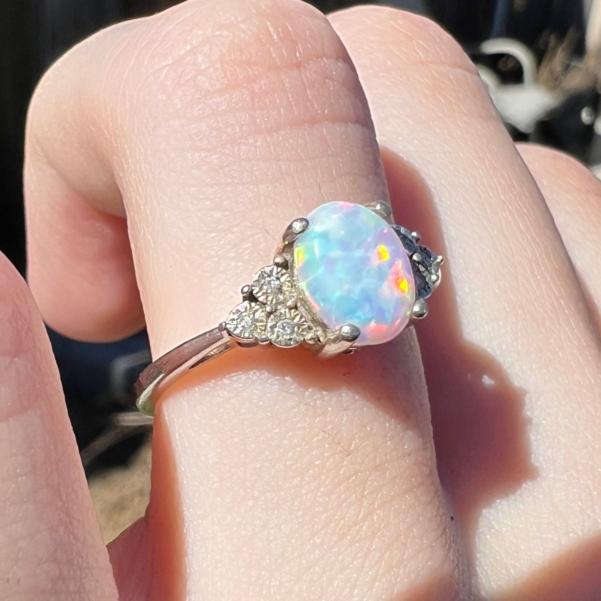 Close-up of used sterling silver lab-created opal and natural diamond ring worn on finger in sunlight.