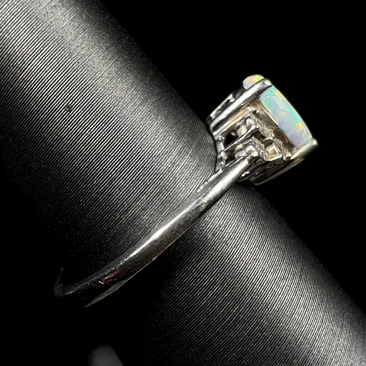 A used sterling silver opal ring viewed from its side shank on a ring display.  Light wear is visible along the surface of the metal.
