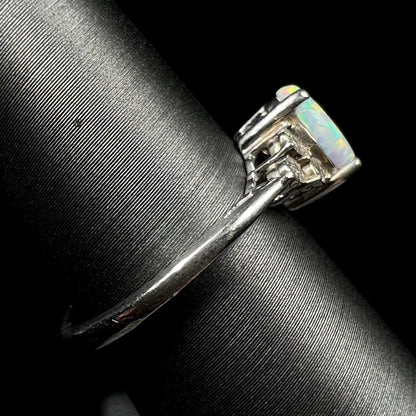 A used sterling silver opal ring viewed from its side shank on a ring display.  Light wear is visible along the surface of the metal.