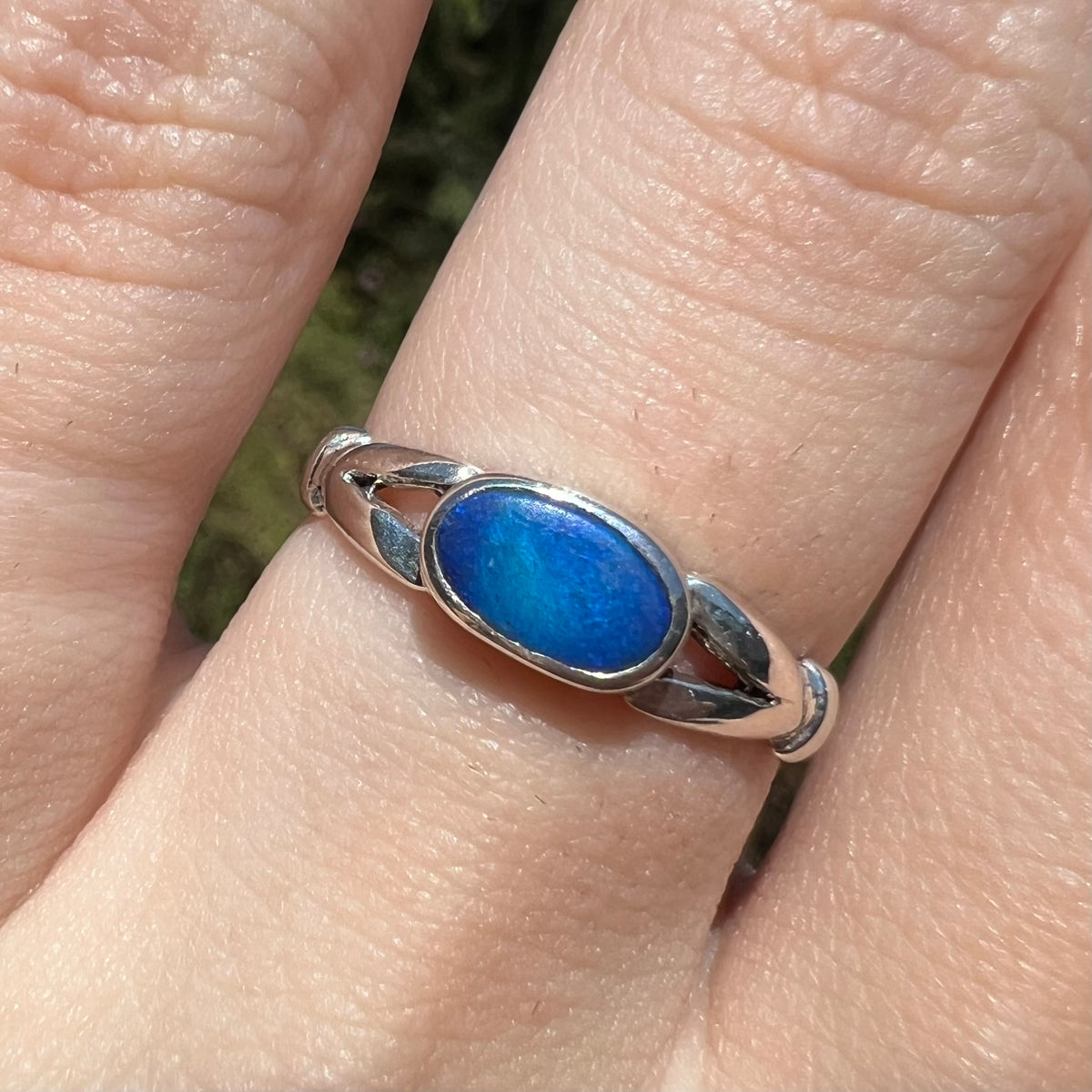 Close-up of used women's sterling silver opal doublet ring with open split shank design, worn on finger in sunlight