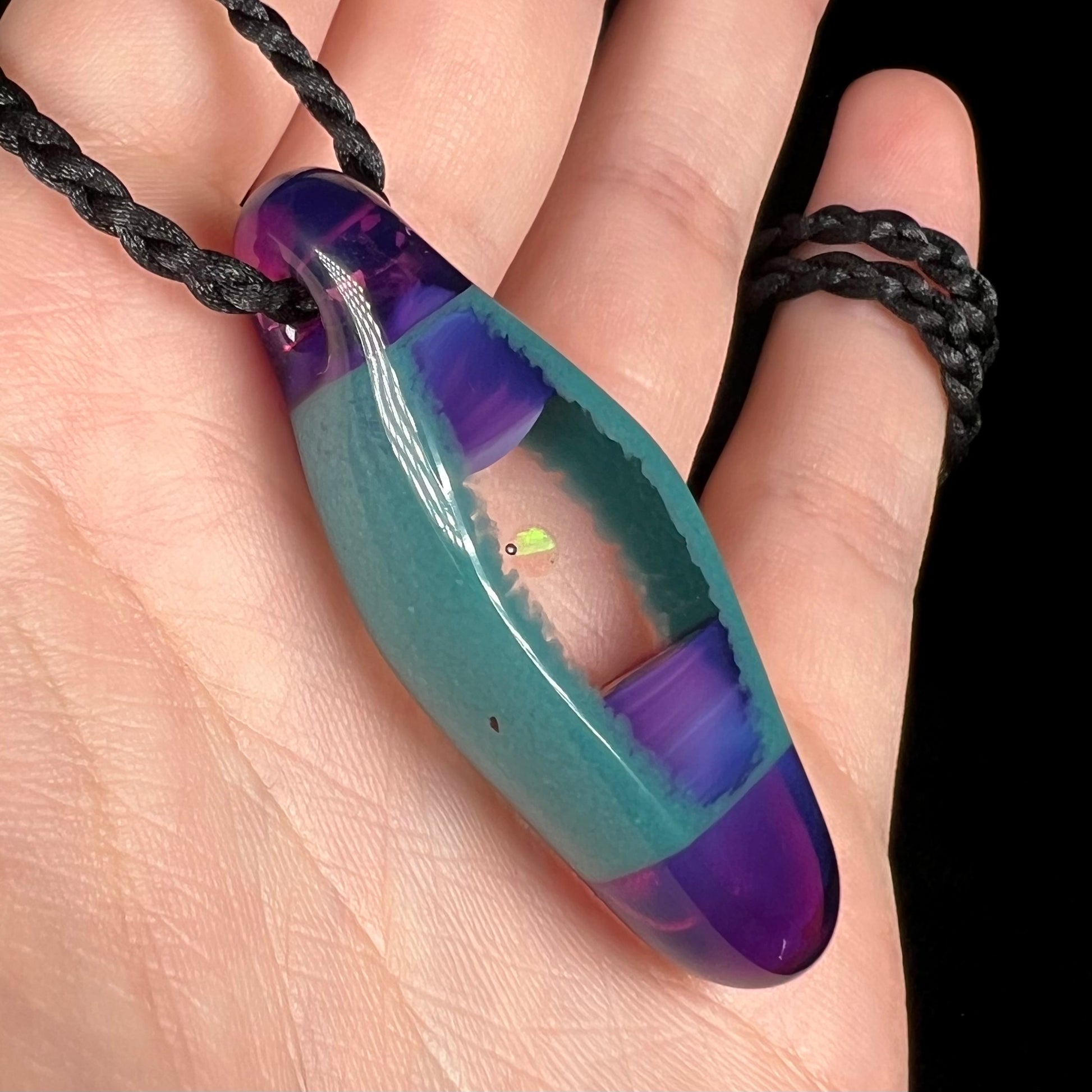 A Utah artist-made boro glass and lab-created opal pendant shown from an angle in a hand close-up.