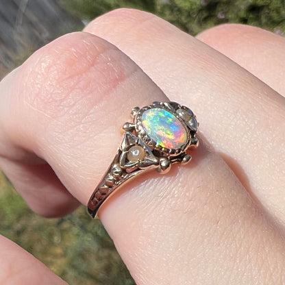 Close-up sunlit view of finger wearing Victorian crystal opal ring in 9k gold with seed pearl accents visible