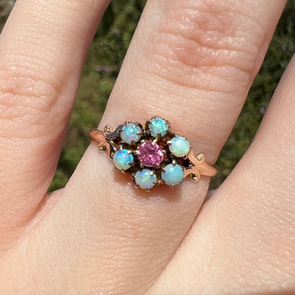 Close-up of 9k gold Victorian ring set with six round Hungarian opals and a pink tourmaline center stone, worn on finger under sunlight