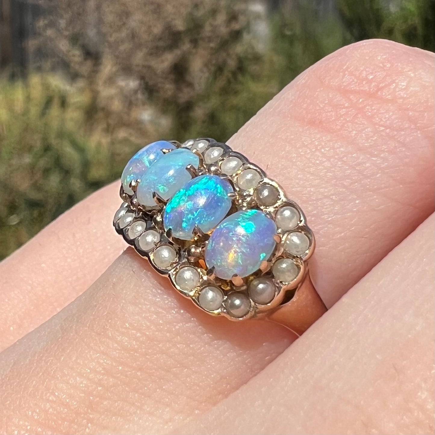 A 9k gold Victorian ring set with four Hungarian opals and seed pearls, shown on finger close-up from angle under sunlight