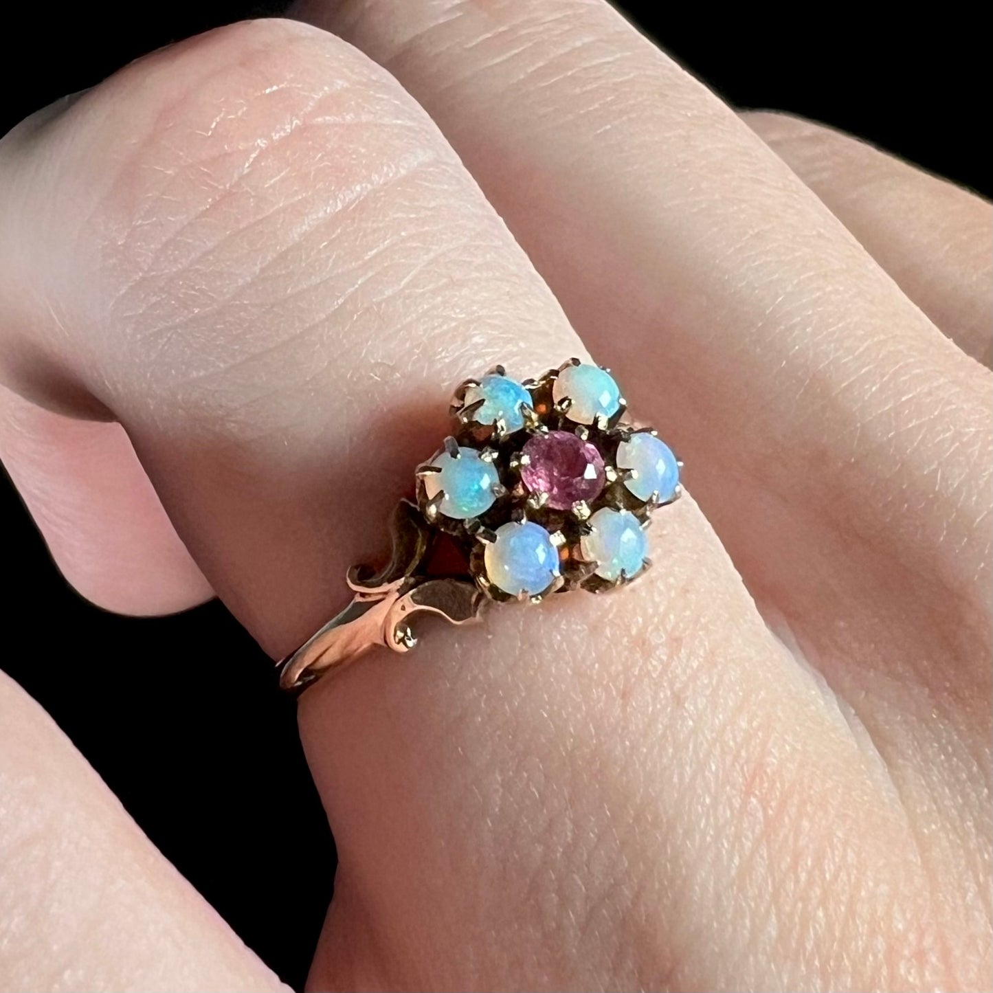 A gold Victorian flower design ring set with cluster of six bluish Hungarian crystal opals and a pink tourmaline center, shown on finger