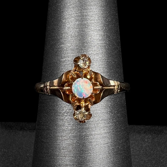 Macro view of antique Victorian three-stone opal and rose cut diamond ring in yellow gold, shown on a ring display against black background.