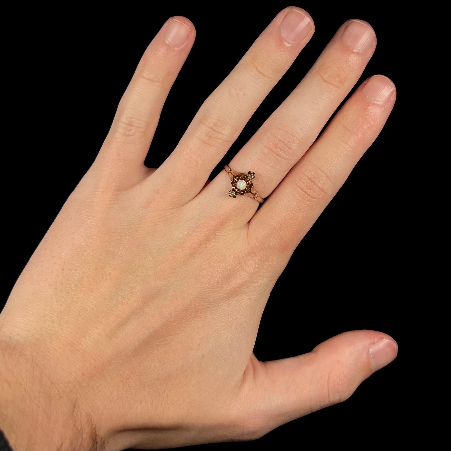 Hand wearing a Victorian three-stone opal and diamond ring in 9k gold under studio light against a black background.