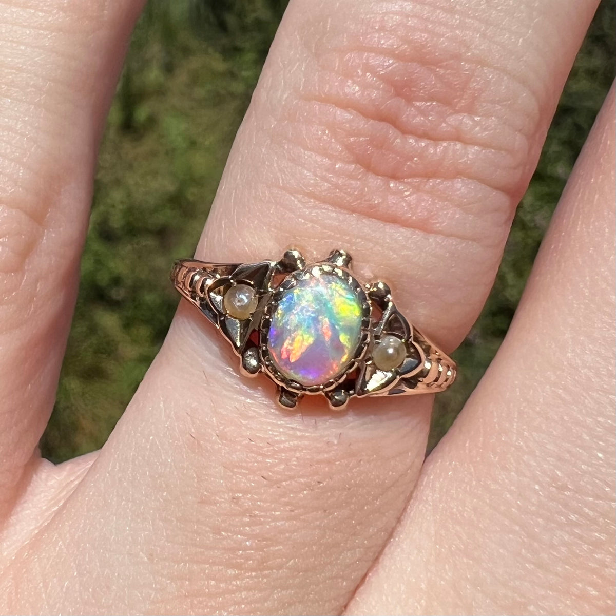 Close-up of colorful Victorian opal and seed pearl engagement ring, worn on finger in sunlight