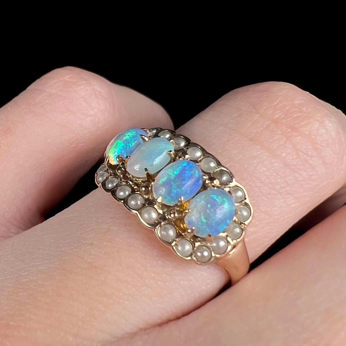 Angled close-up of 9k gold Victorian opal and seed pearl ring, worn on finger