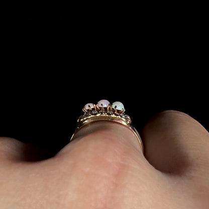 Side profile gallery view of a Victorian three-stone opal ring worn on a hand, the ring's many gold prongs in focus