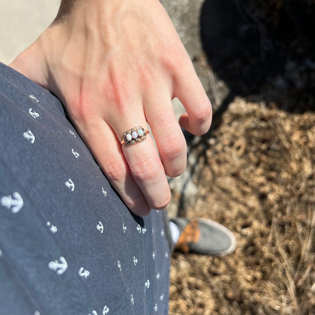 Person's hand resting on hip in sunlight wearing a 9k gold Victorian ring set with three opals surrounded by halo of seed pearls