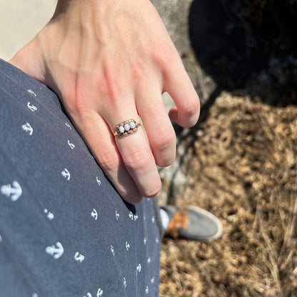 Person's hand resting on hip in sunlight wearing a 9k gold Victorian ring set with three opals surrounded by halo of seed pearls