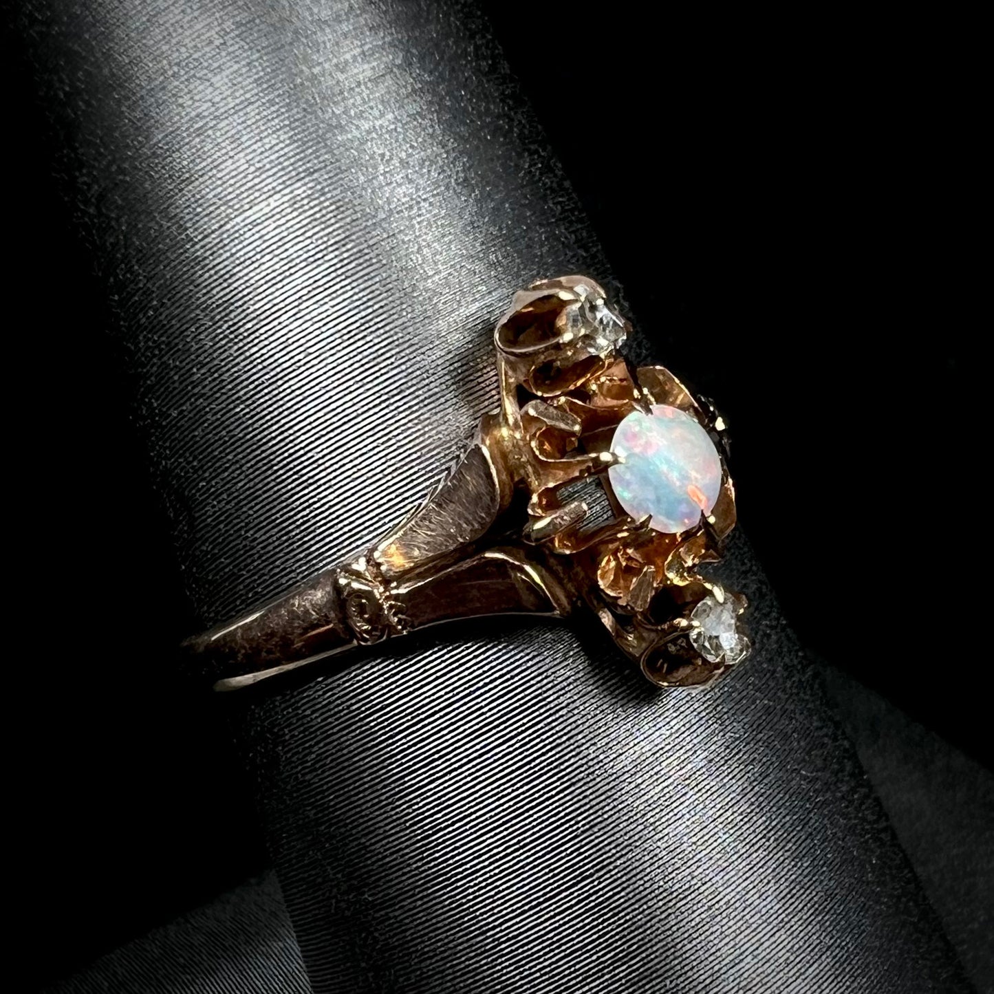 Angled close-up of a Victorian opal and rose cut diamond ring shown on a ring display against a black backdrop.