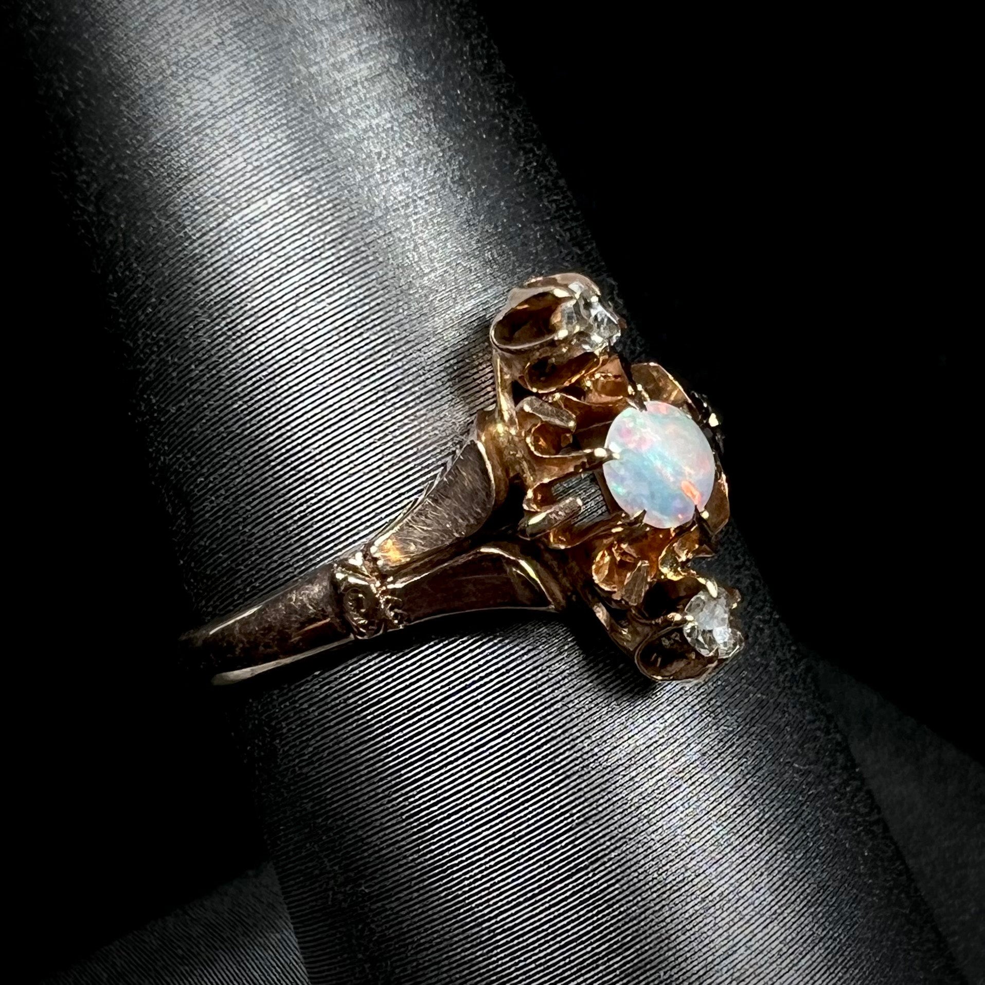 Angled close-up of a Victorian opal and rose cut diamond ring shown on a ring display against a black backdrop.
