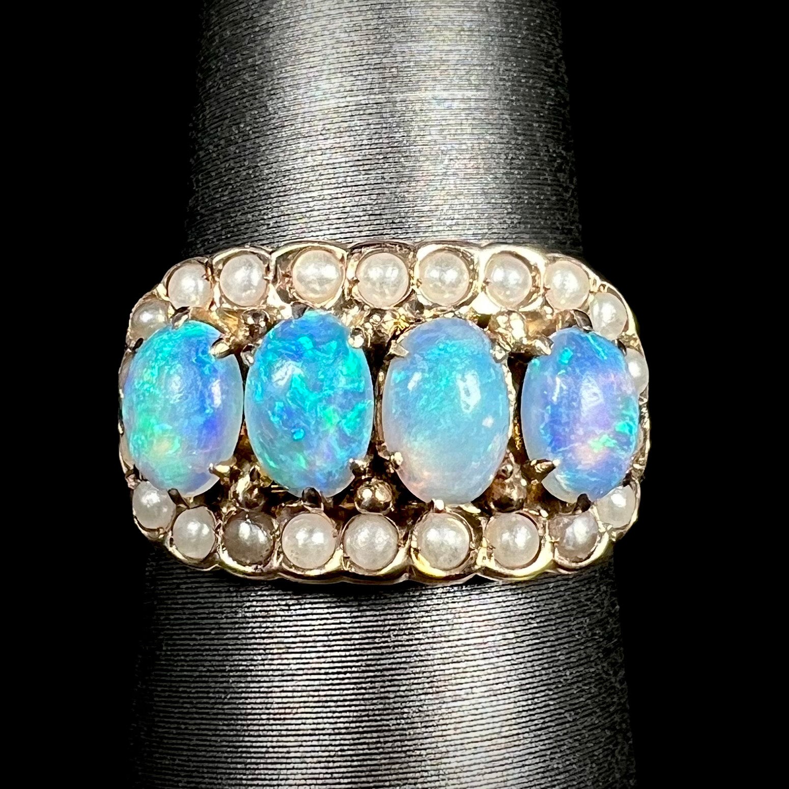 Close-up of Victorian four-stone opal and seed pearl halo ring in 9k gold, shown on ring display