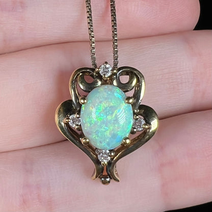Close-up of a reproduction-era Victorian style opal and CZ pendant in patinaed gold-tone metal, held on fingers.