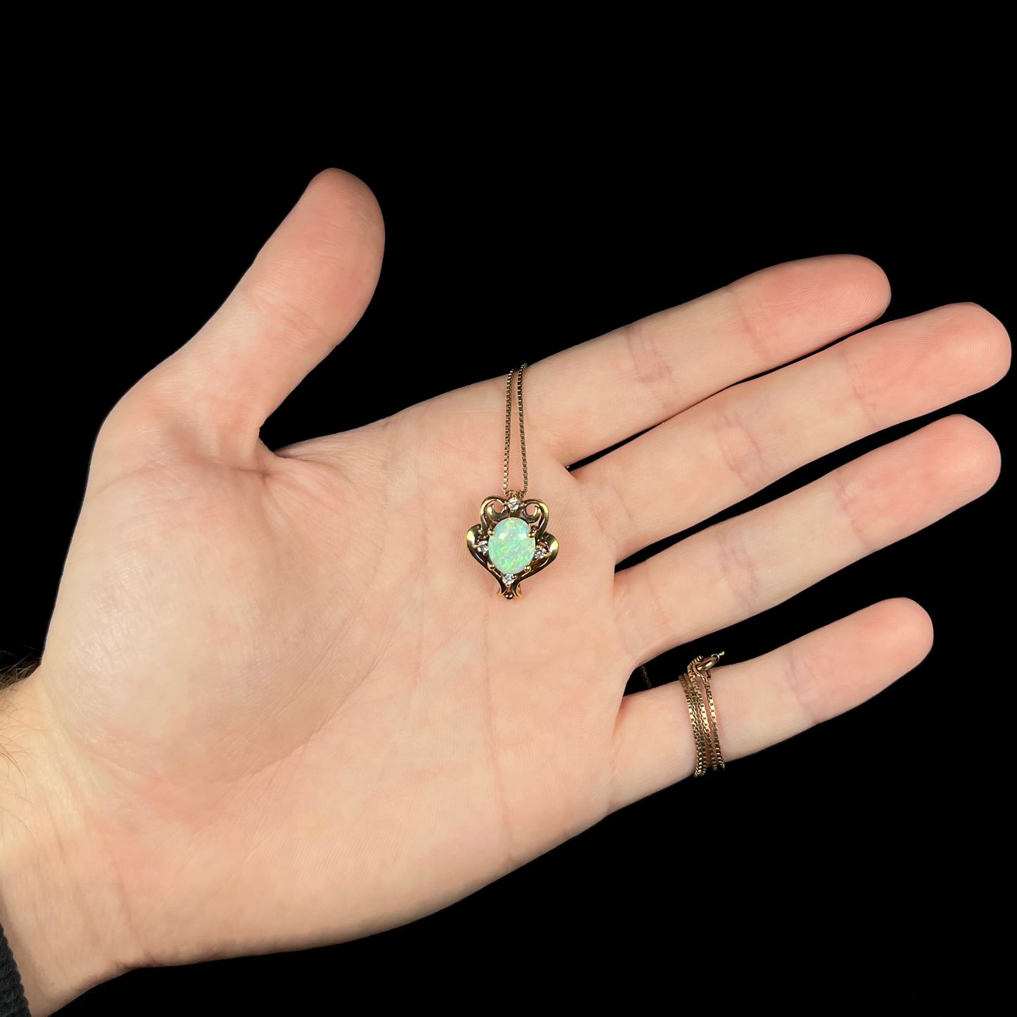 Hand holding a vintage Victorian-style lab opal and CZ necklace beneath LED studio lights.