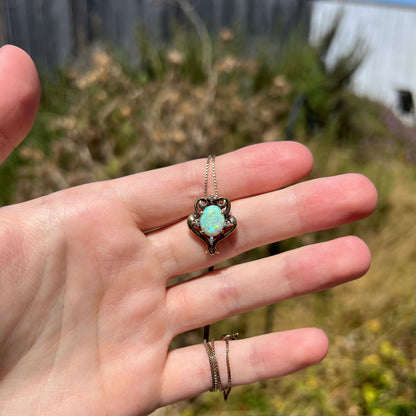 Hand holding a women's Victorian-style oval-shaped opal and CZ necklace in sunlight against a blurred outdoor background.