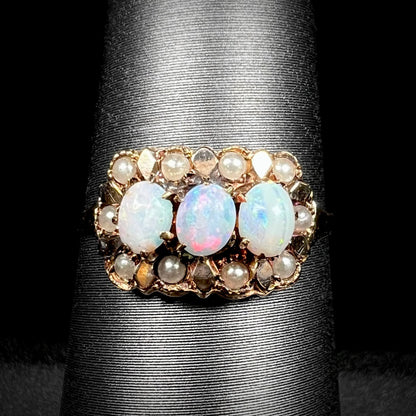 Close-up of a late Victorian era three-stone Australian opal and seed pearl-accented ring in 9k gold, shown on ring display