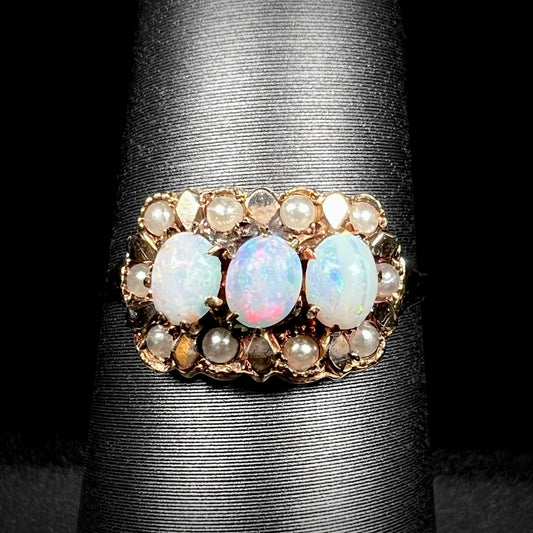 Close-up of a late Victorian era three-stone Australian opal and seed pearl-accented ring in 9k gold, shown on ring display