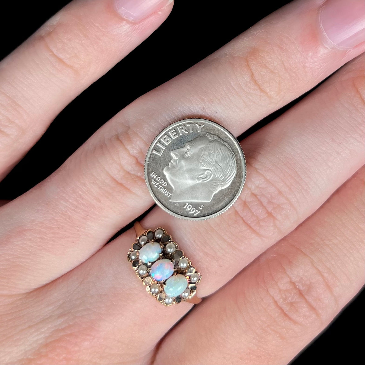 Close-up of hand wearing a Victorian era three-stone opal ring with seed pearl halo; a US dime coin is resting on hand next to ring for scale
