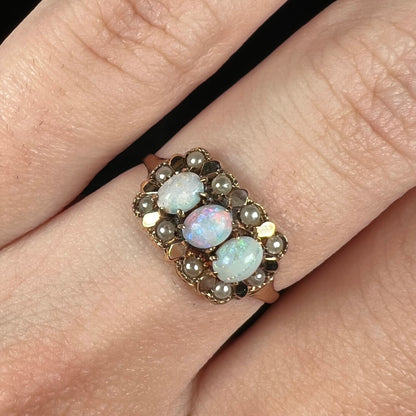 Close-up of three-stone Victorian ring set with White Cliffs opals and a halo of seed pearl accents in 9k gold, worn on a finger