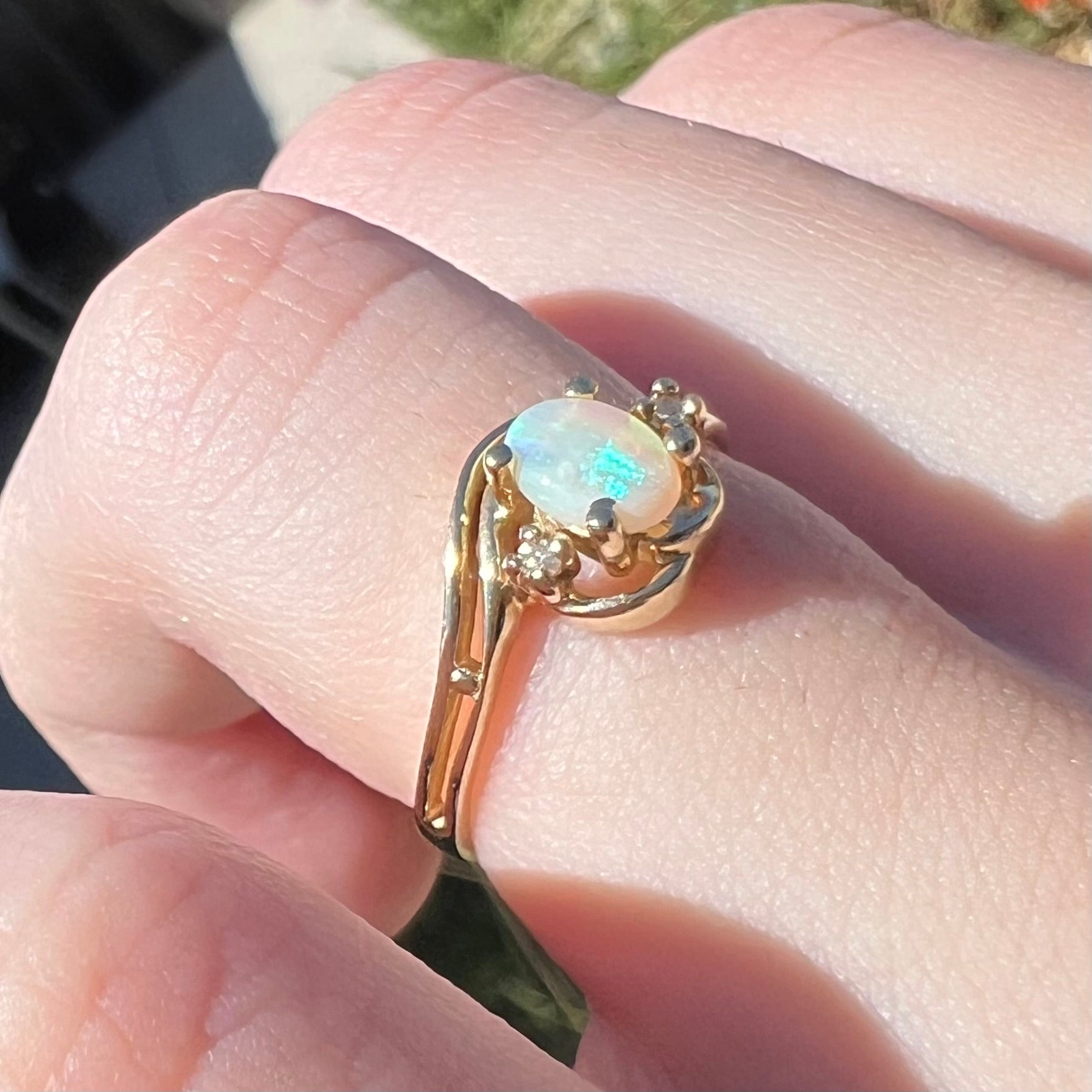Close-up angled view of a vintage 10k gold Australian opal and diamond engagement ring with split-shank design, shown in sunlight.