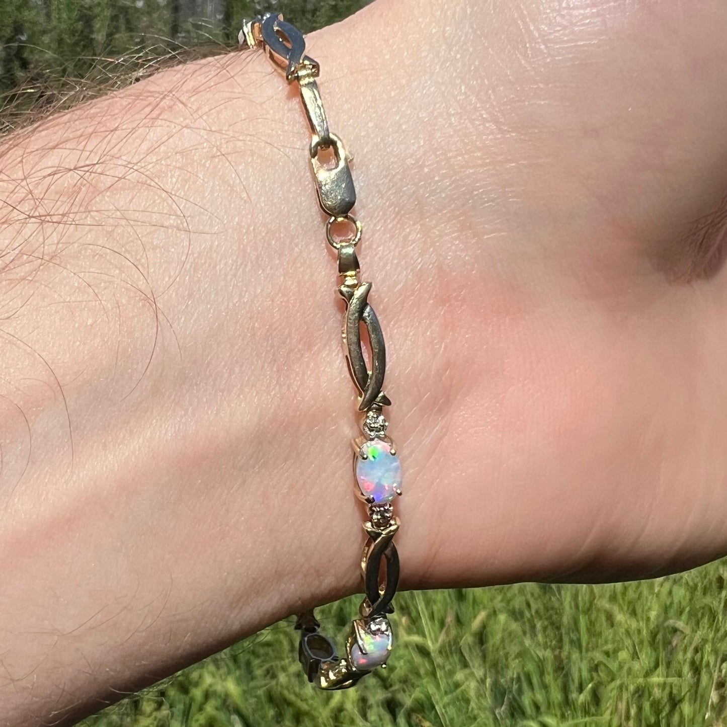 Vintage 10k gold bracelet with lobster clasp and oval cut lab-created opals shown on wrist from underside in sunlight.