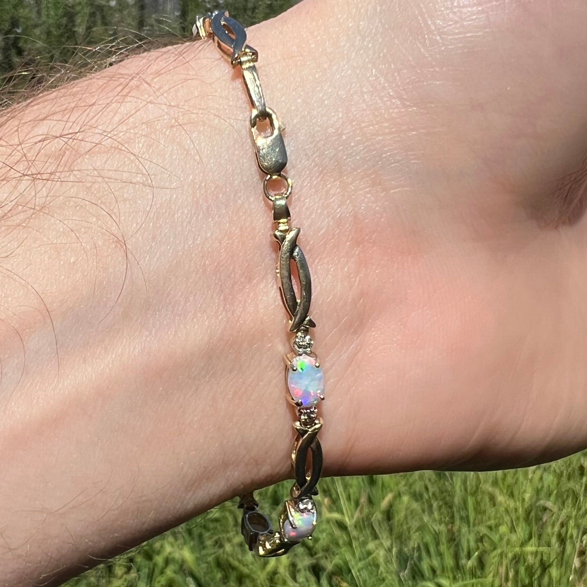 Vintage 10k gold bracelet with lobster clasp and oval cut lab-created opals shown on wrist from underside in sunlight.