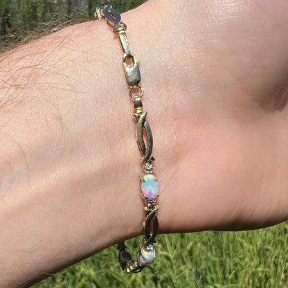 Vintage 10k gold bracelet with lobster clasp and oval cut lab-created opals shown on wrist from underside in sunlight.