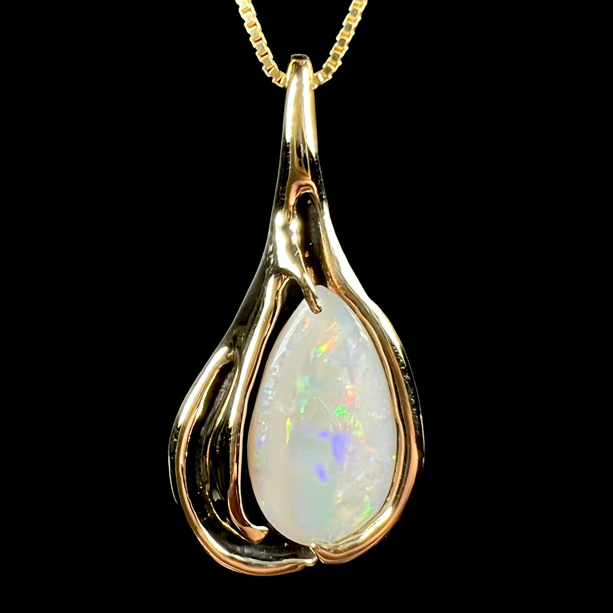 Close-up front view of a vintage 14k yellow gold opal solitaire pendant with Modernist design and black antiquing, shown on chain against black background