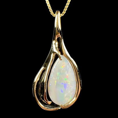 Close-up front view of a vintage 14k yellow gold opal solitaire pendant with Modernist design and black antiquing, shown on chain against black background